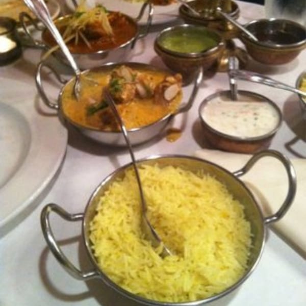 Indian dishes including yellow rice, chicken curry, and various chutneys in metal bowls on a table.