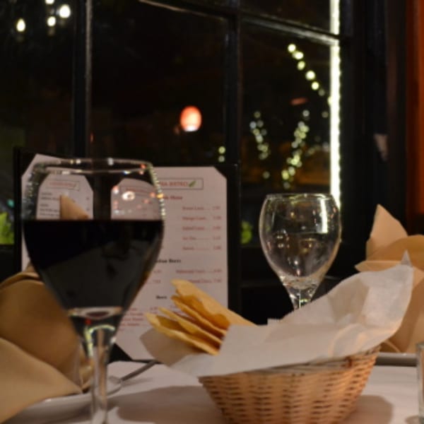 Table setting at Batika India Bistro with red wine, water glass, and bread basket.