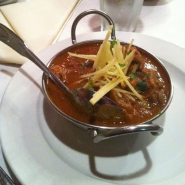 Indian curry in a metal bowl with a spoon, garnished with ginger and herbs.
