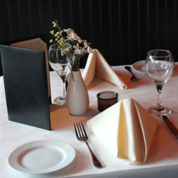 A set table at Batika India Bistro with white plates, napkins, wine glasses, and a menu.