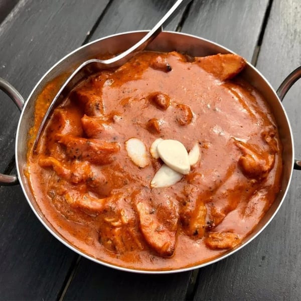 A metal bowl of Batika India Bistro's butter chicken, garnished with almond slivers.