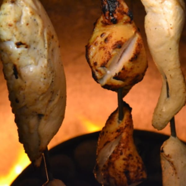 Chicken pieces on skewers cooking in a tandoor oven, with a fiery orange glow.