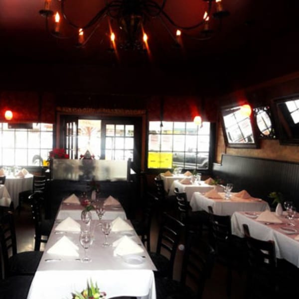 The dimly lit dining room of Batika India Bistro, with tables set with white tablecloths and dark chairs.