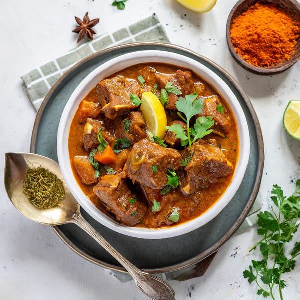 Indian lamb curry with lemon, cilantro, and spices, served in a white bowl on a grey plate.