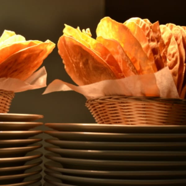Two baskets of crispy Indian papadum, with stacks of plates below, at Batika India Bistro.