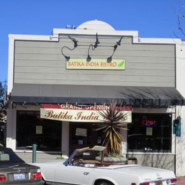 Exterior of Batika India Bistro with a "Grand Opening" banner and cars parked in front.