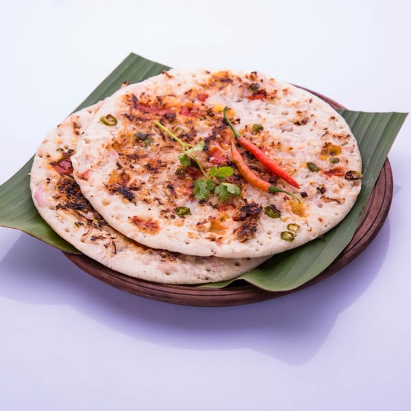 Two Indian uttapam pancakes with vegetables, cilantro, and red chilies on banana leaves.