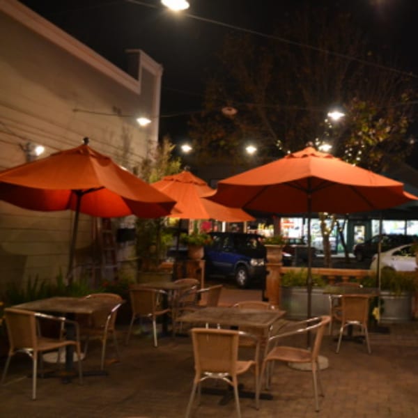 Batika India Bistro's outdoor patio at night, with orange umbrellas, tables, and chairs.