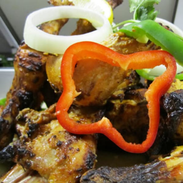 Close-up of grilled Indian chicken with red bell pepper, onion, and green chili garnish.