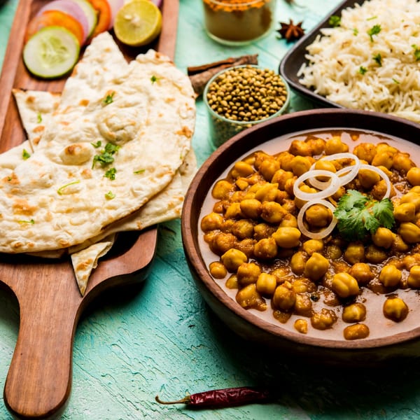 Batika India Bistro's chana masala with naan, rice, and fresh vegetables on a blue table.