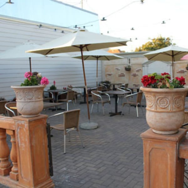 Outdoor patio at Batika India Bistro with tables, chairs, umbrellas, and potted flowers.