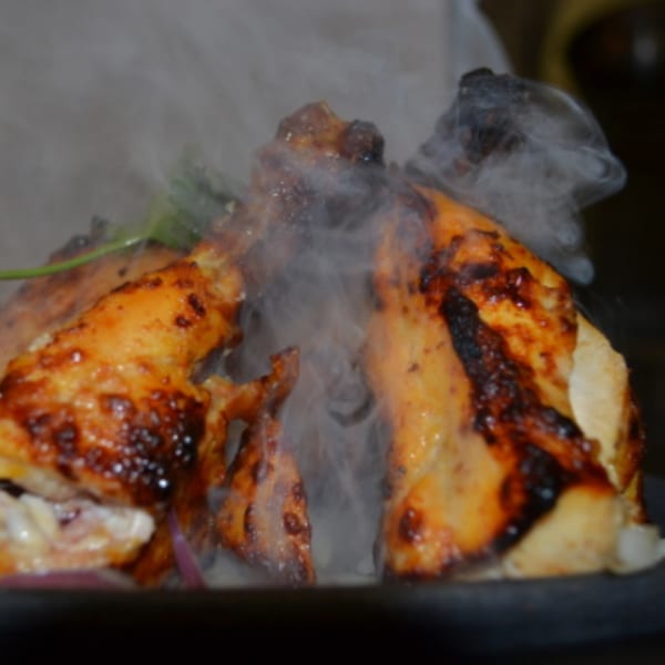 Sizzling Indian chicken dish with smoke rising, garnished with fresh herbs and onions.
