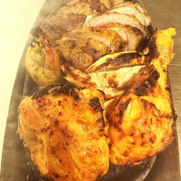 Sizzling platter of Indian grilled meats, including sliced beef, chicken pieces, and a prawn.