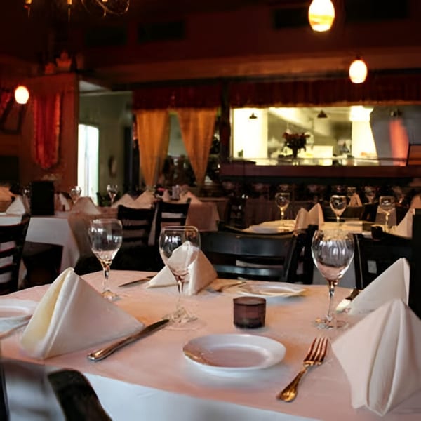 Elegantly set tables with white tablecloths, wine glasses, and napkins in a dimly lit Indian bistro.