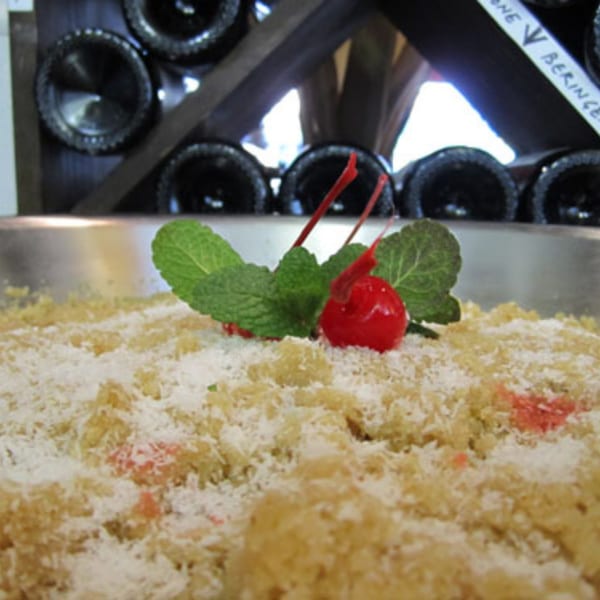Indian dessert with shredded coconut, garnished with mint and a cherry, in front of wine bottles.