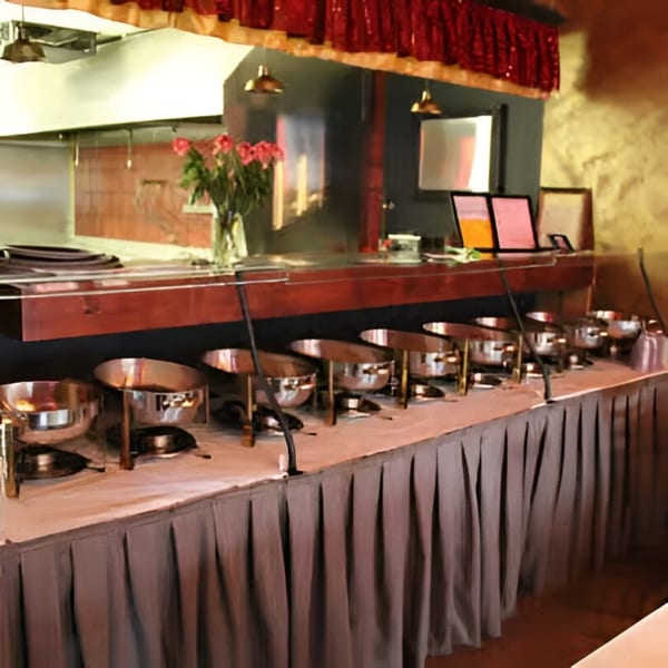 A long buffet table with multiple silver chafing dishes and a vase of pink roses.